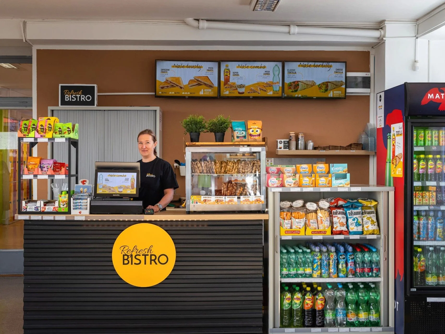 Prodejní pult školního bistra s menu na obrazovkách a chladicími vitrínami