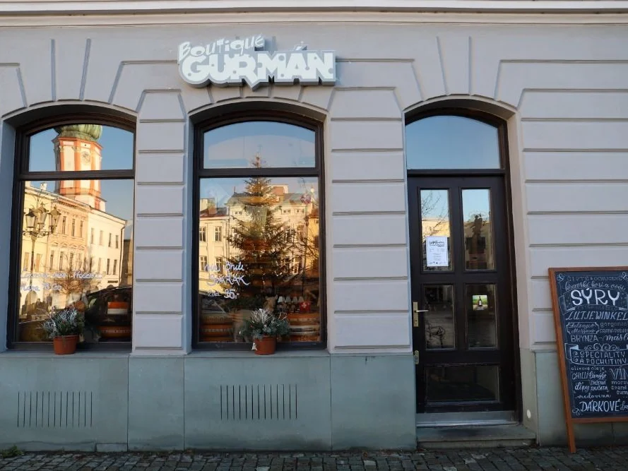 Prodejna v historické budově na náměstí, výloha s tabulí a nápisem Boutique Gurmán